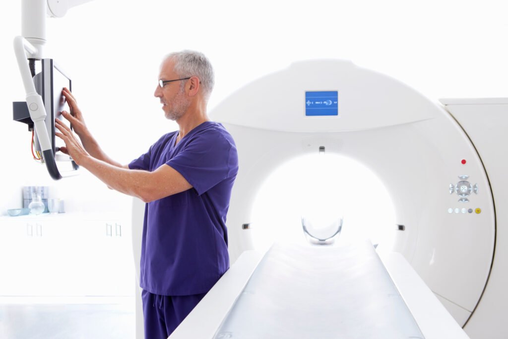 Clinician in scrubs using the control screen of a CT scanner in a hospital imaging room