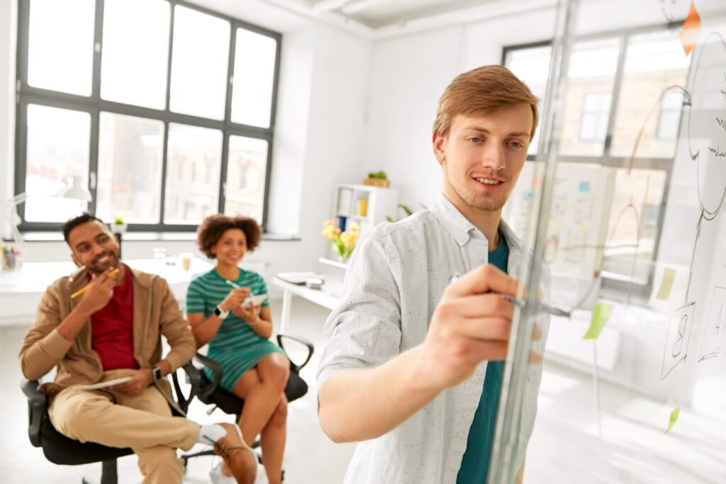 Engineer sketching a system diagram on a glass board while two colleagues watch