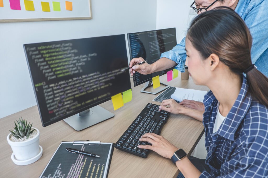 Two software developers reviewing code together on dual monitors